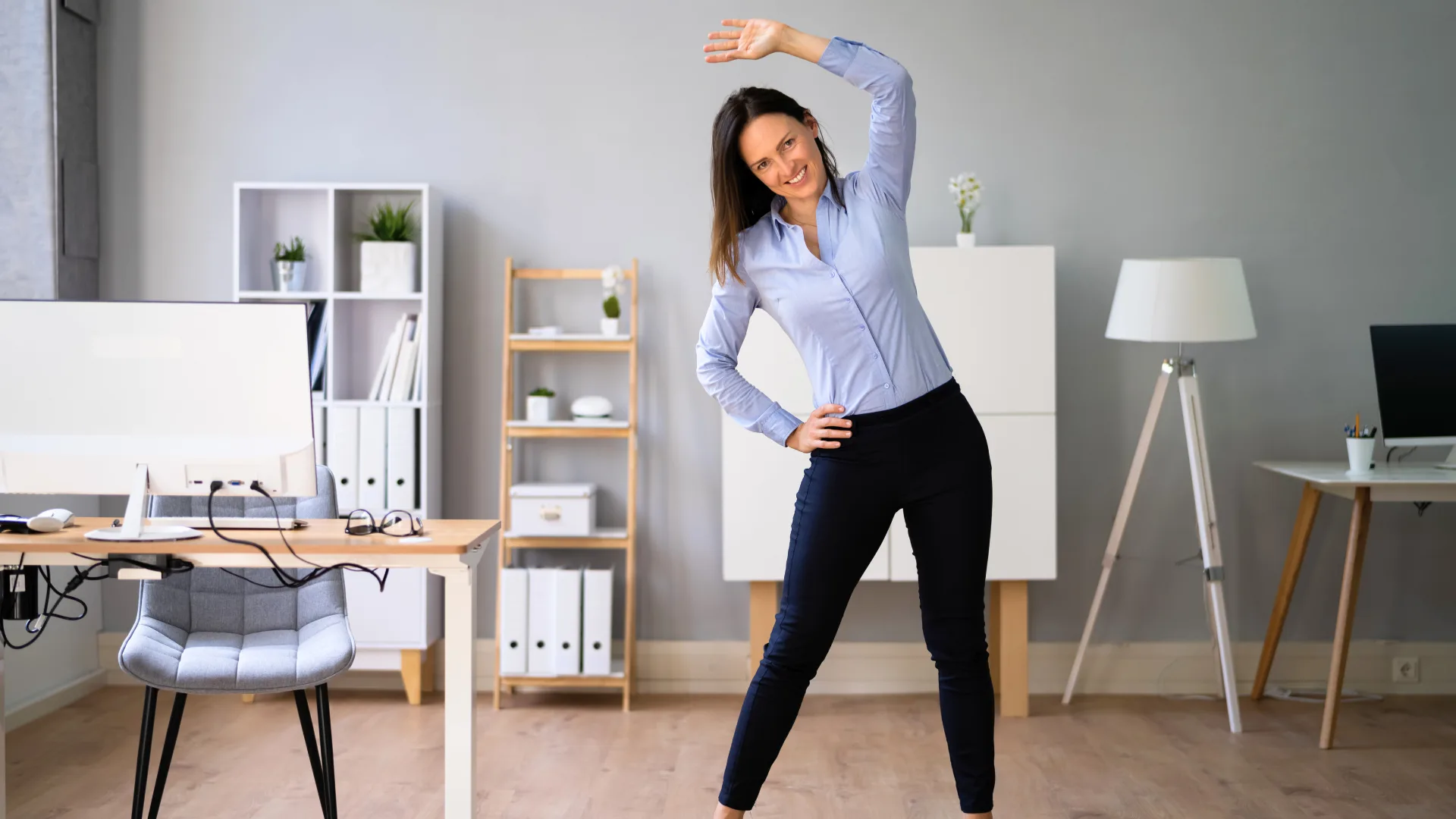 Home office sem dor: 5 alongamentos para aliviar dores e tensões em minutos 3 Mulher se alongando no escritório durante a rotina de home office para melhorar o bem-estar e evitar dores.
