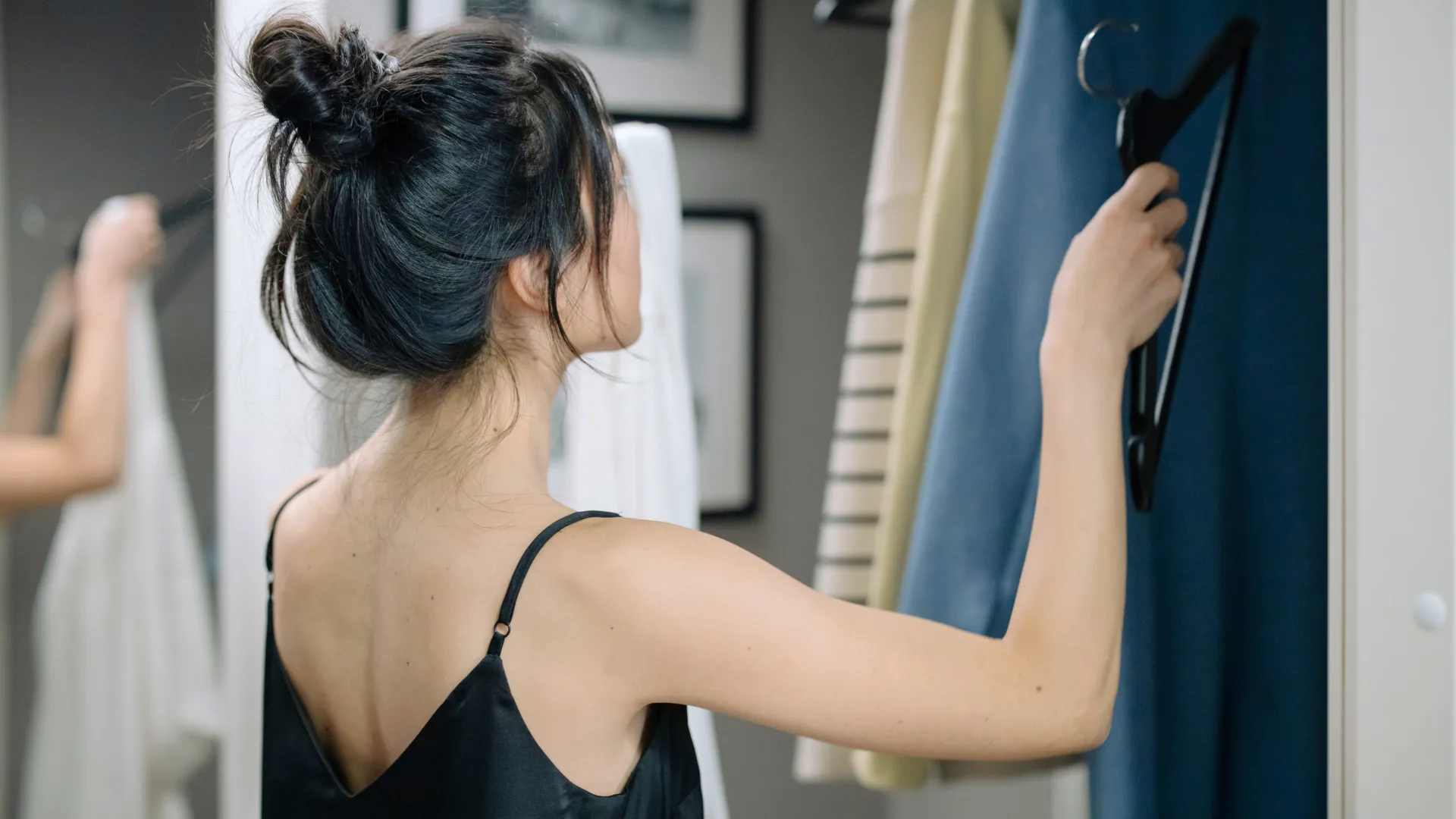 mulher-roupa-trabalho-home-office-importancia.jpg Mulher selecionando peças de roupa no guarda-roupa para trabalho home office, destacando a importância da roupa no desempenho profissional.