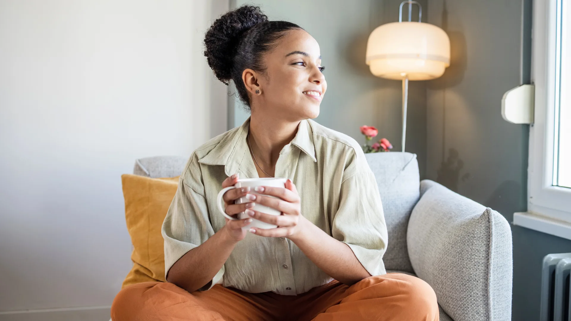 Produtividade ou armadilha? Os riscos de ignorar pausas no home office 3 Mulher em pausa produtiva no home office, tomando café e olhando pela janela com semblante sereno, espairecendo a mente.