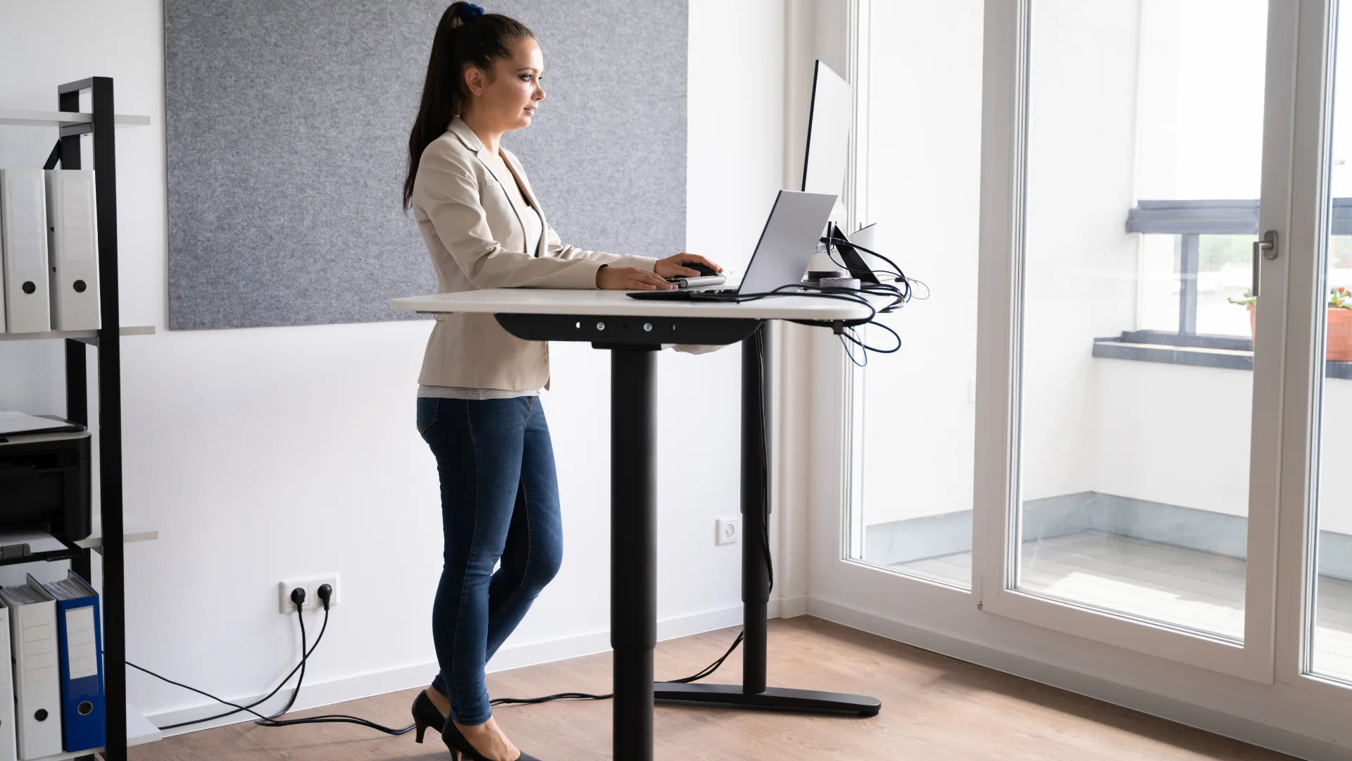 3 itens pouco comentados que estão transformando o home office de quem trabalha sério 3 Profissional utilizando mesa regulável em pé, trabalhando com notebook e monitor em um ambiente de home office moderno e bem iluminado