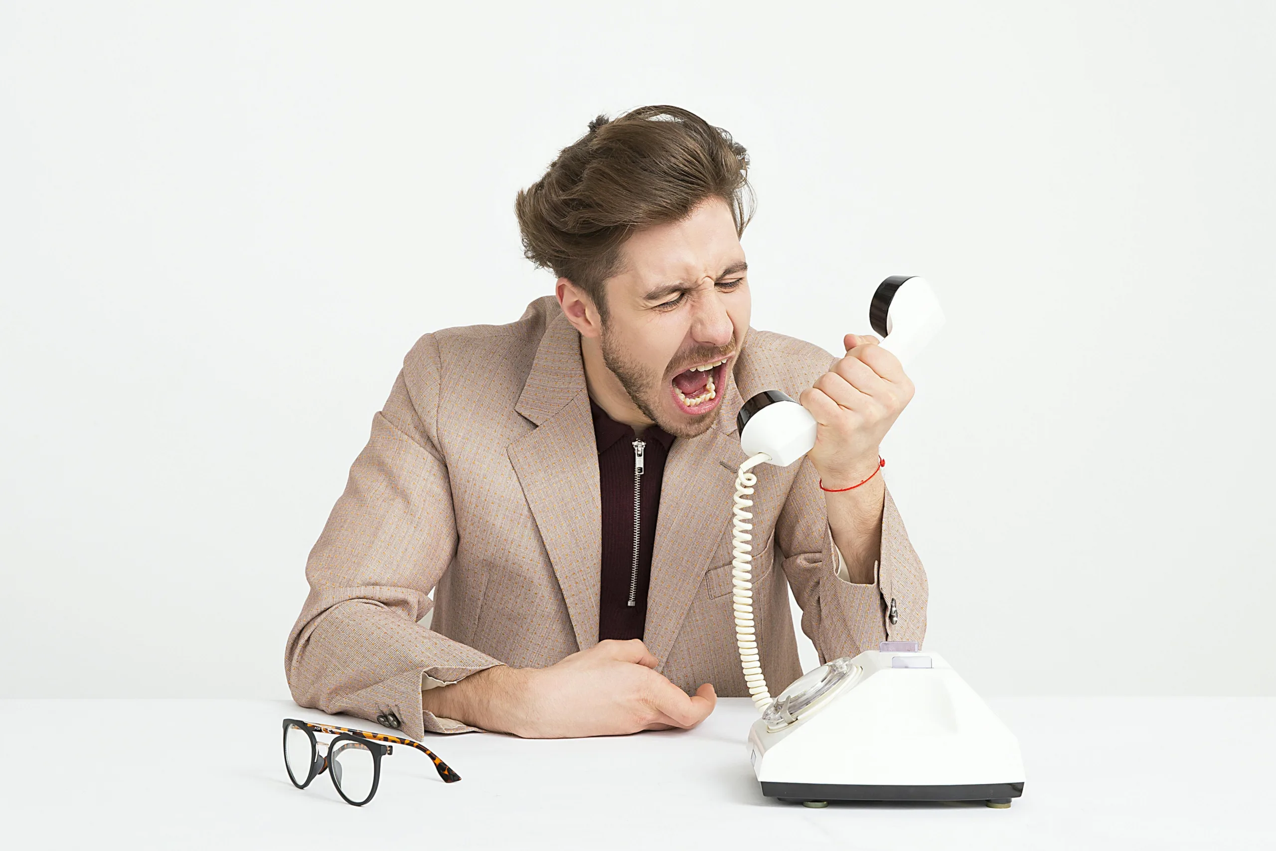 Desafios do Home Office: A verdade que ninguém te conta 3 Empresário de terno bege gritando em um telefone antigo, expressando frustração no trabalho.